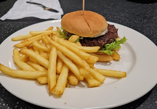 A burger and fries served on a white plate positioned on a dark, speckled counter top.