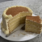 A tall, multi-layered cake with a slice removed sits on a white plate