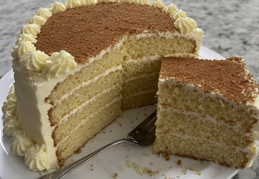 A tall, multi-layered cake with a slice removed sits on a white plate