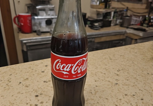 A glass bottle of Coca-Cola positioned on a speckled counter top