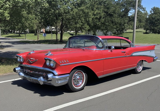 A full-shot, eye-level outdoor photograph of a vintage red Chevrolet Bel Air, likely from 1957