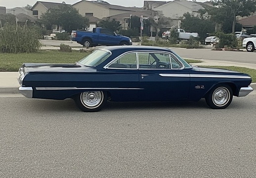 A classic, dark blue two-door coupe parked on a paved street in a suburban setting. 