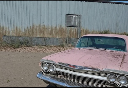 A vintage pink car parked in front of a dilapidated building. 