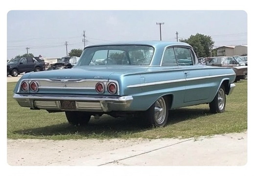 A classic light blue two-door sedan parked on a grassy area next to a dirt path. 